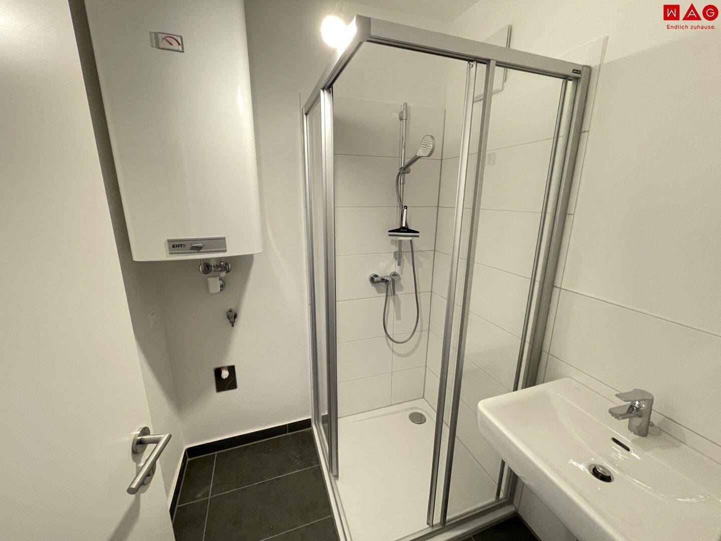 Modernes Badezimmer mit Duschkabine, Waschbecken und einem Wandboiler für Warmwasser.