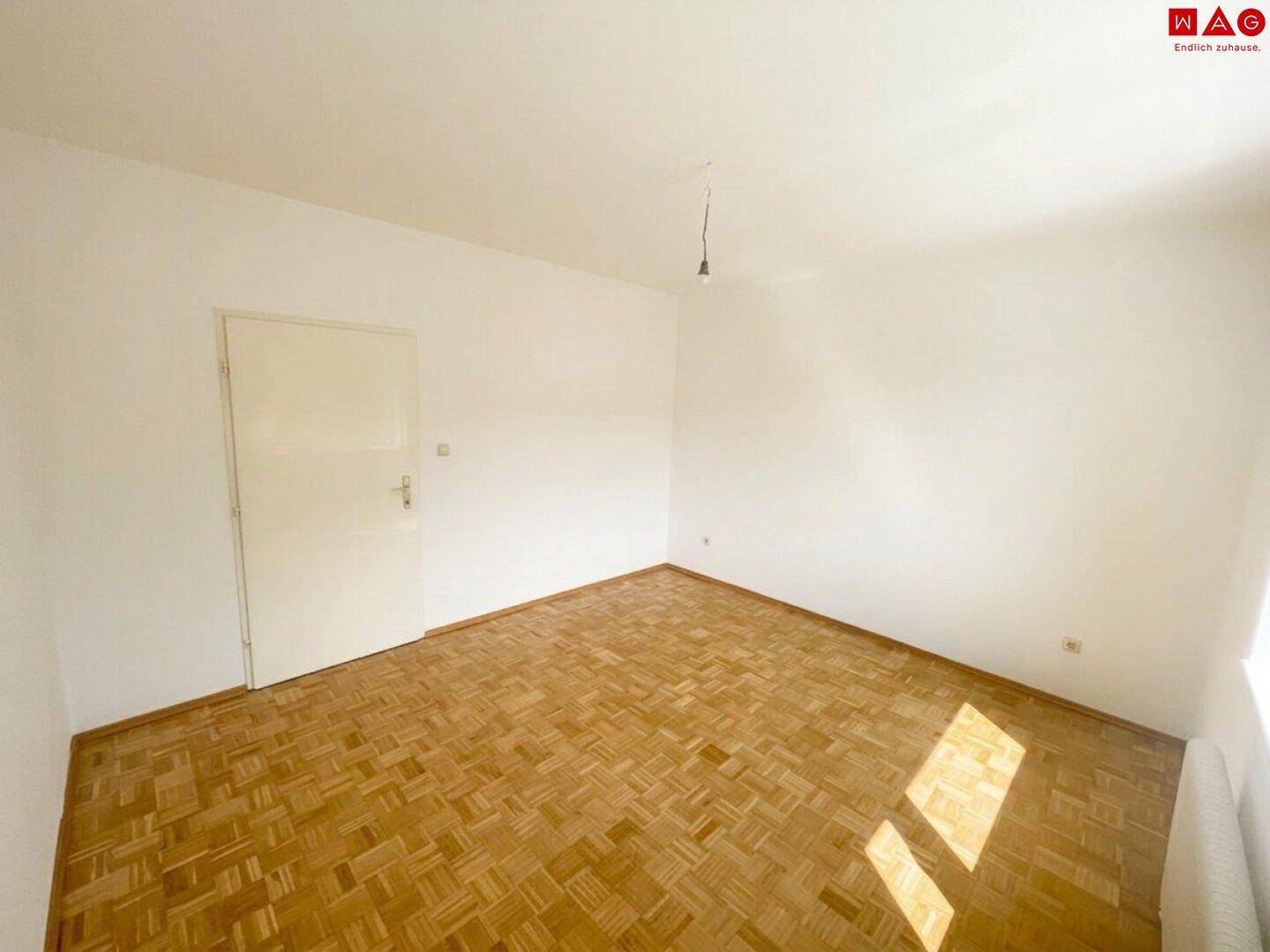 Helles Schlafzimmer mit Parkettboden und weiß gestrichenen Wänden.