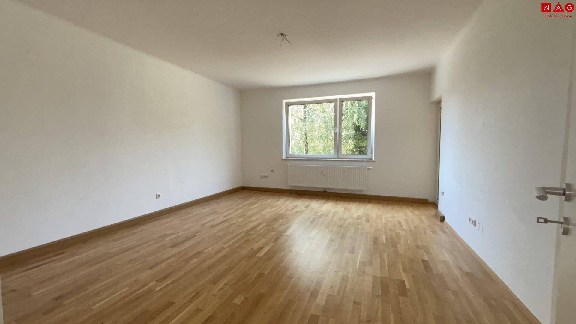 Helles Wohnzimmer mit neuwertigem Parkettboden und Blick ins Grüne.