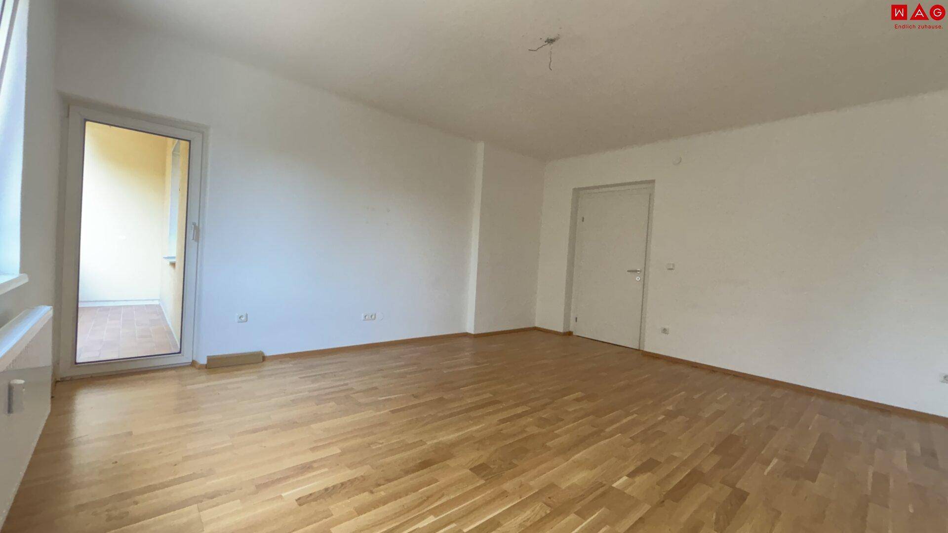 Geräumiges Wohnzimmer mit Parkettboden und Zugang zum Balkon.