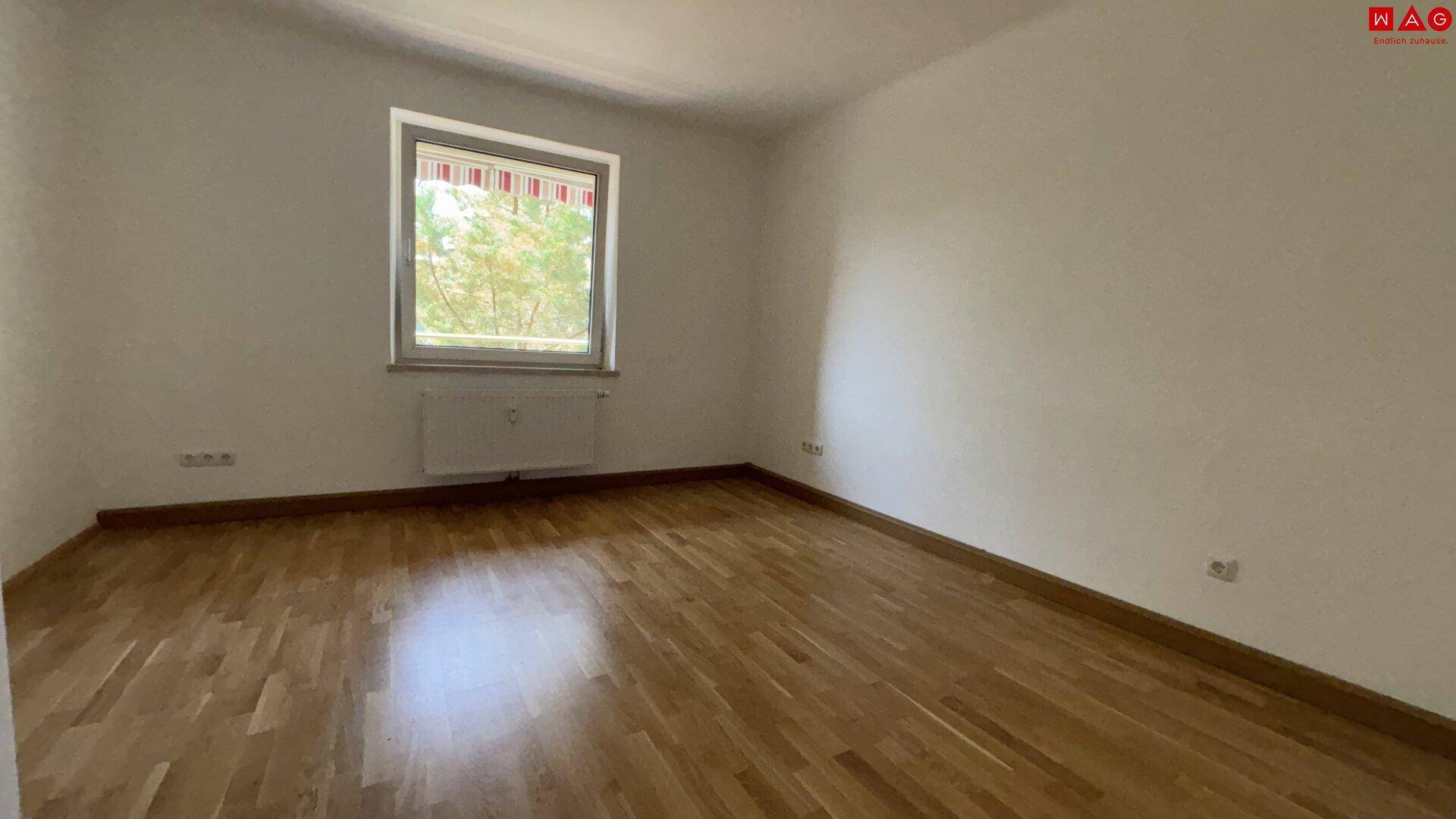 Schlafzimmer mit Parkettboden und Fenster, das viel Tageslicht hereinlässt.
