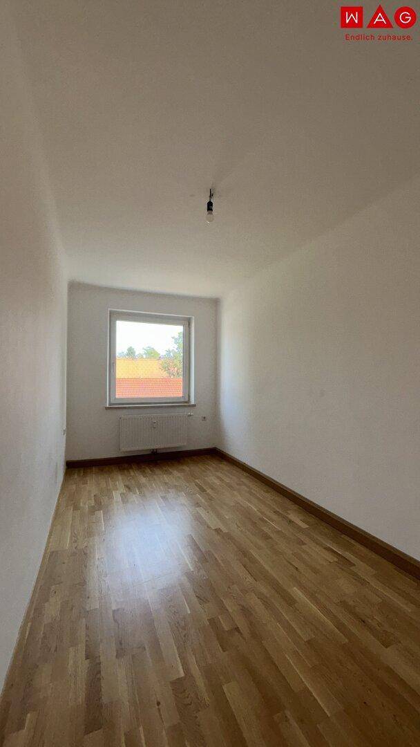 Helles Schlafzimmer mit Parkettboden und einem Fenster mit Blick nach draußen.
