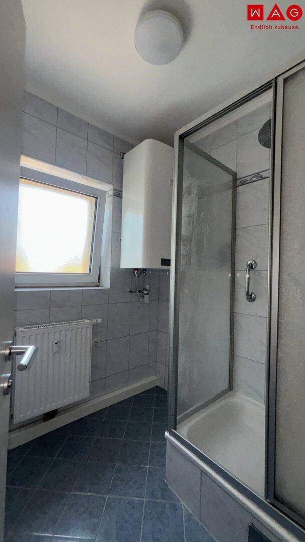 Badezimmer mit Duschkabine, Fenster und hellen Fliesen.