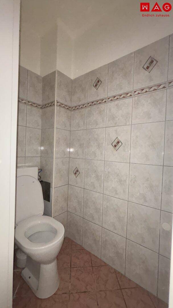 Separate Toilette mit hellen Fliesen und einfacher Ausstattung.