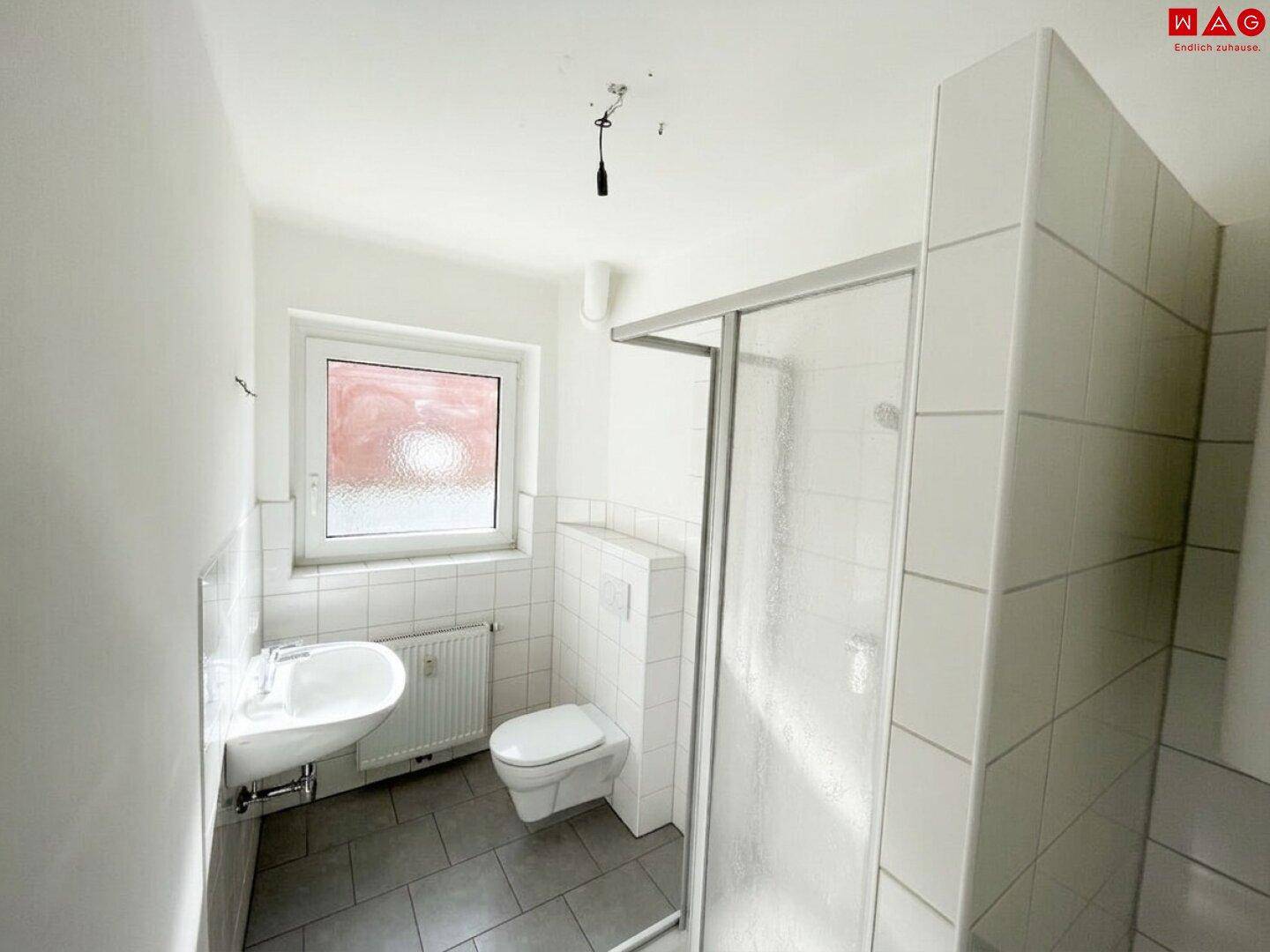 Funktionales Badezimmer mit Duschkabine, WC, Waschbecken und einem Fenster für Tageslicht.