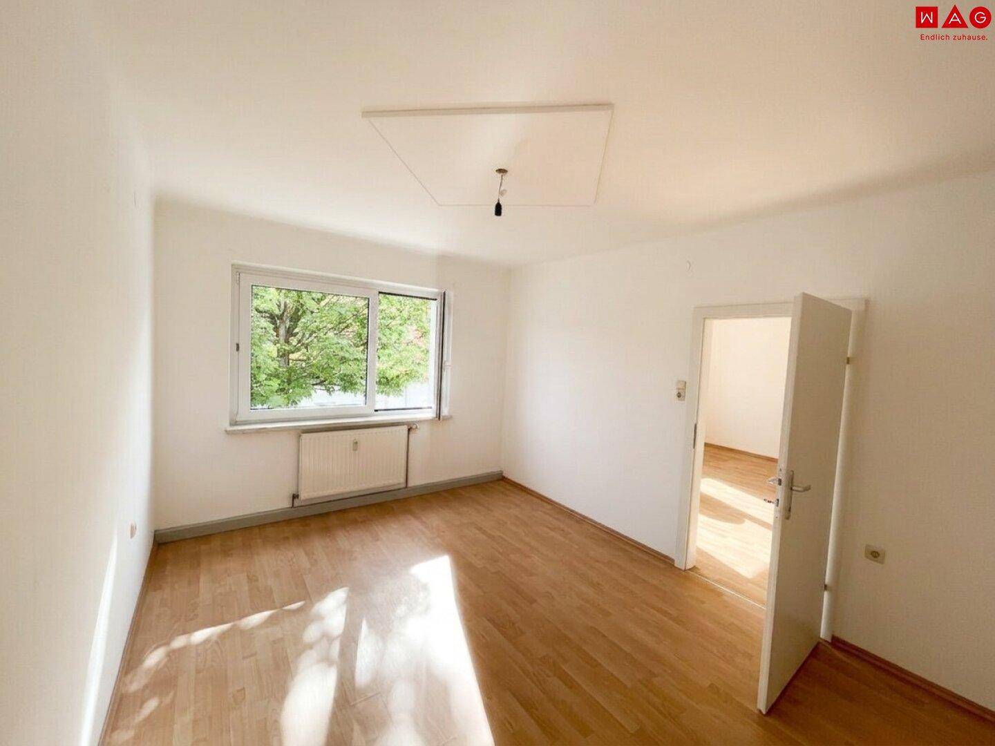 Geräumiges Zimmer mit Holzboden, großen Fenstern und viel Tageslicht, bereit zur Einrichtung.