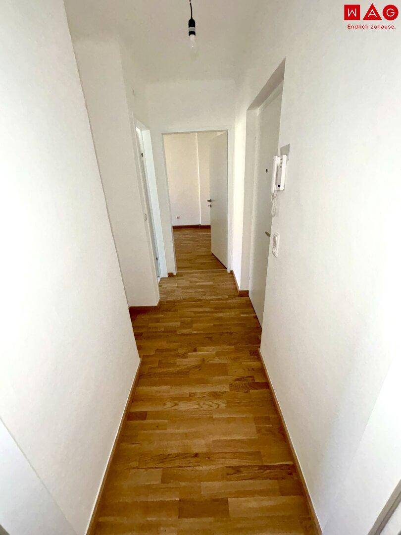Heller Flur mit neu verlegtem Parkettboden, der zu weiteren Räumen führt.
