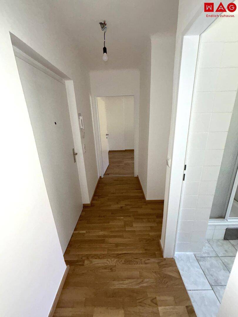 Eingangsbereich mit Holzparkett und Blick in den gefliesten Badezimmerbereich.