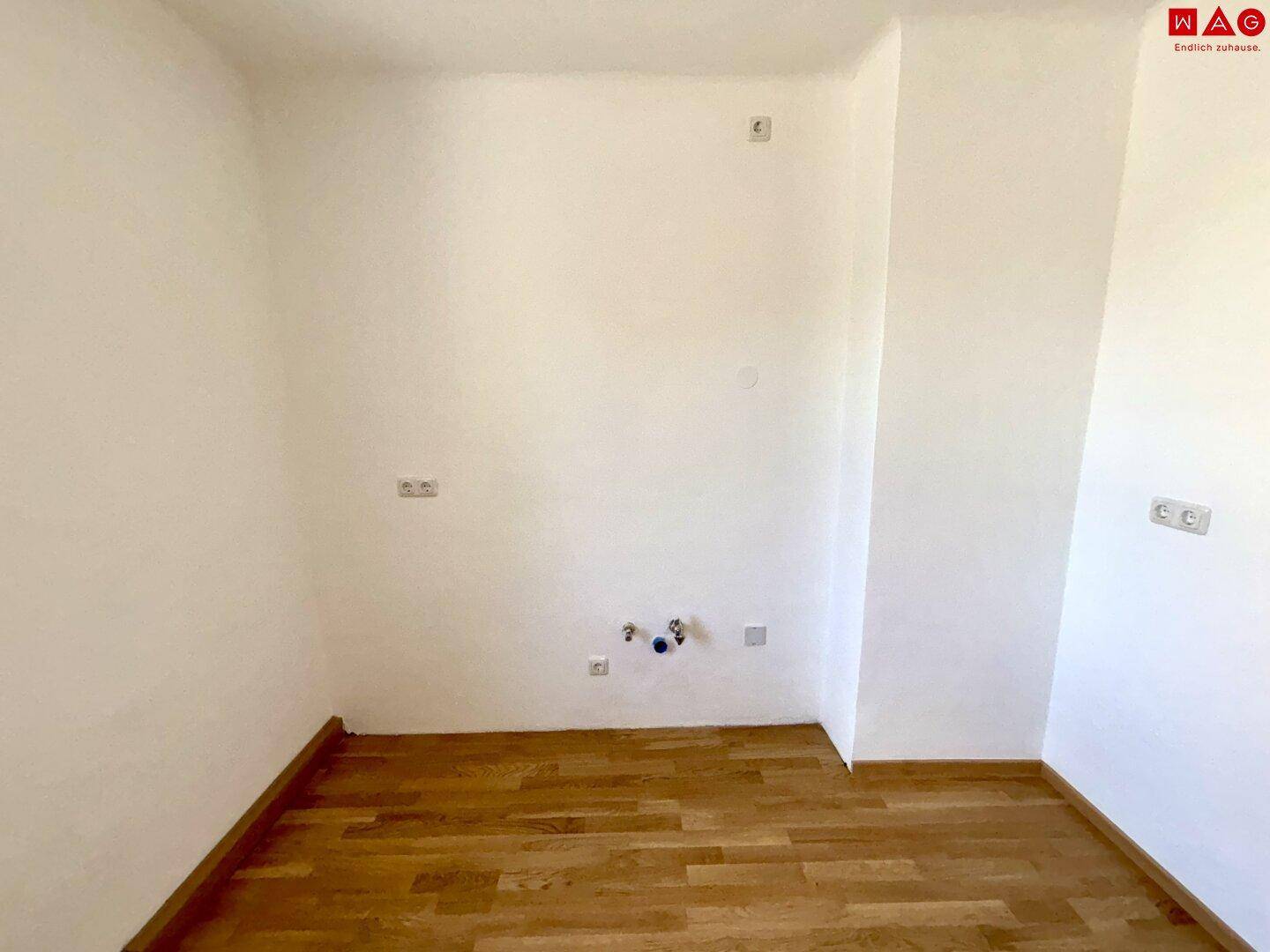 Leerer Raum mit Parkettboden und Anschlüssen, möglicherweise für eine Küche vorgesehen.