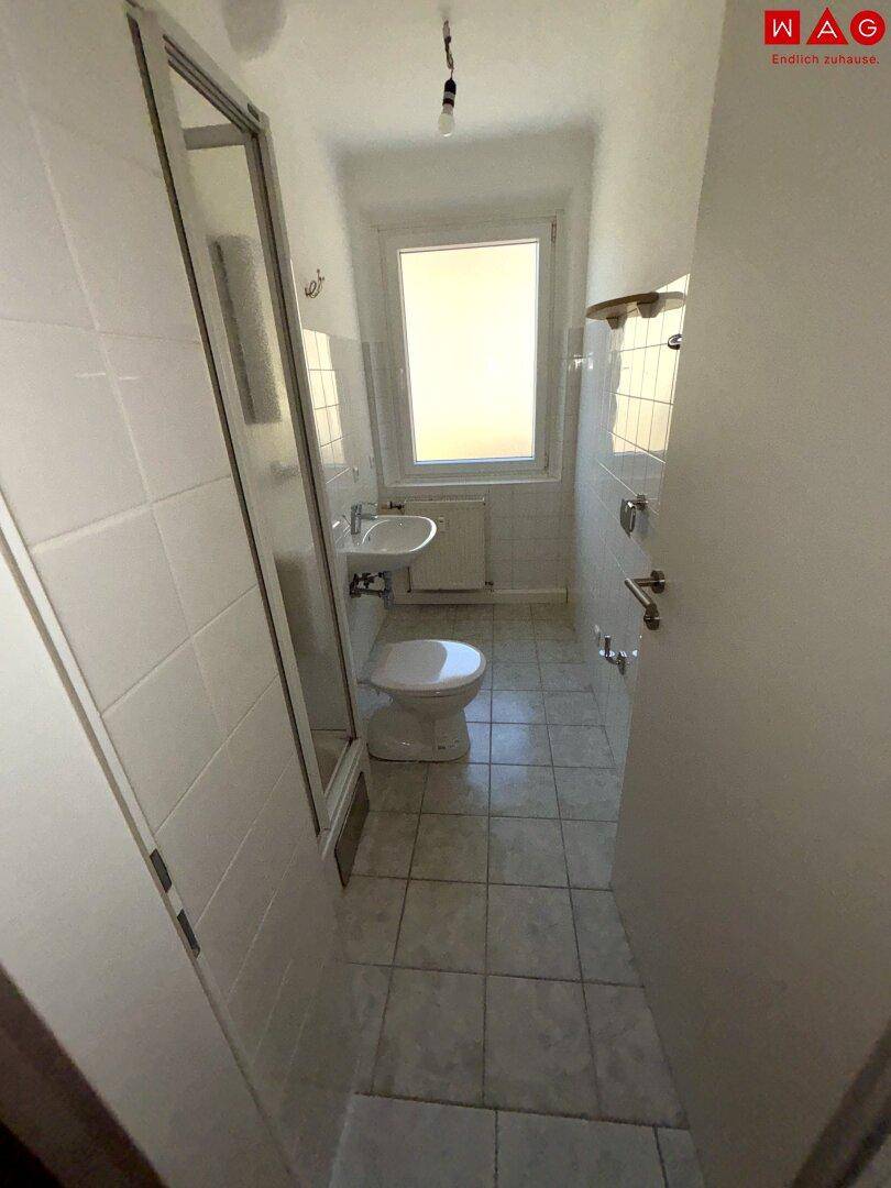 Kleines Badezimmer mit Dusche, WC und Fenster für natürliche Belüftung.