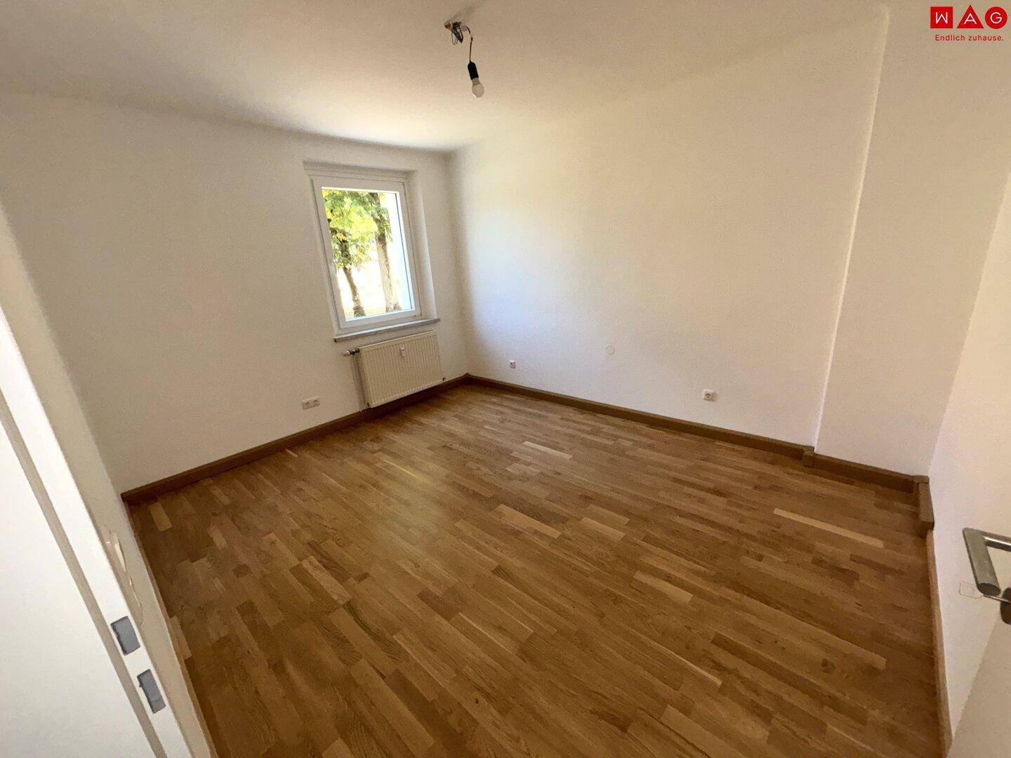 Helles Zimmer mit Parkettboden und Blick ins Grüne, ideal als Schlaf- oder Kinderzimmer.