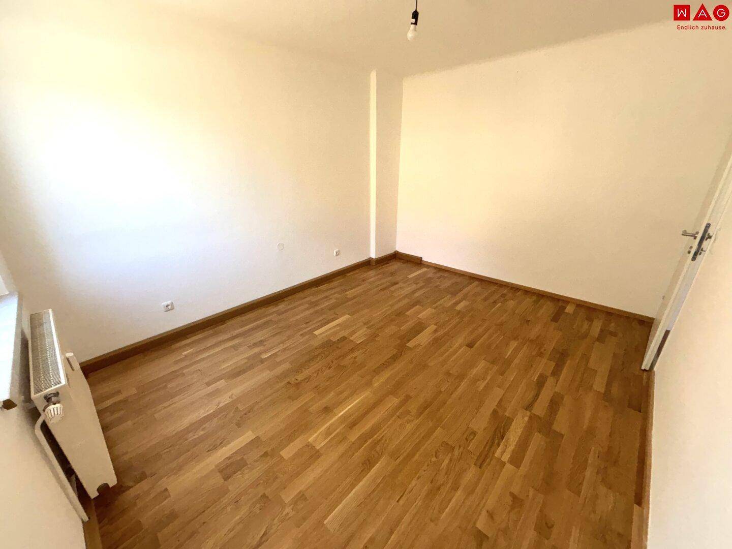 Lichtdurchflutetes Zimmer mit Parkettboden und Heizkörper unter dem Fenster.