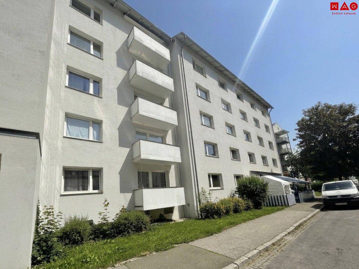 Mehrstöckiges Wohngebäude mit zahlreichen Balkonen und weißer Fassade unter blauem Himmel.