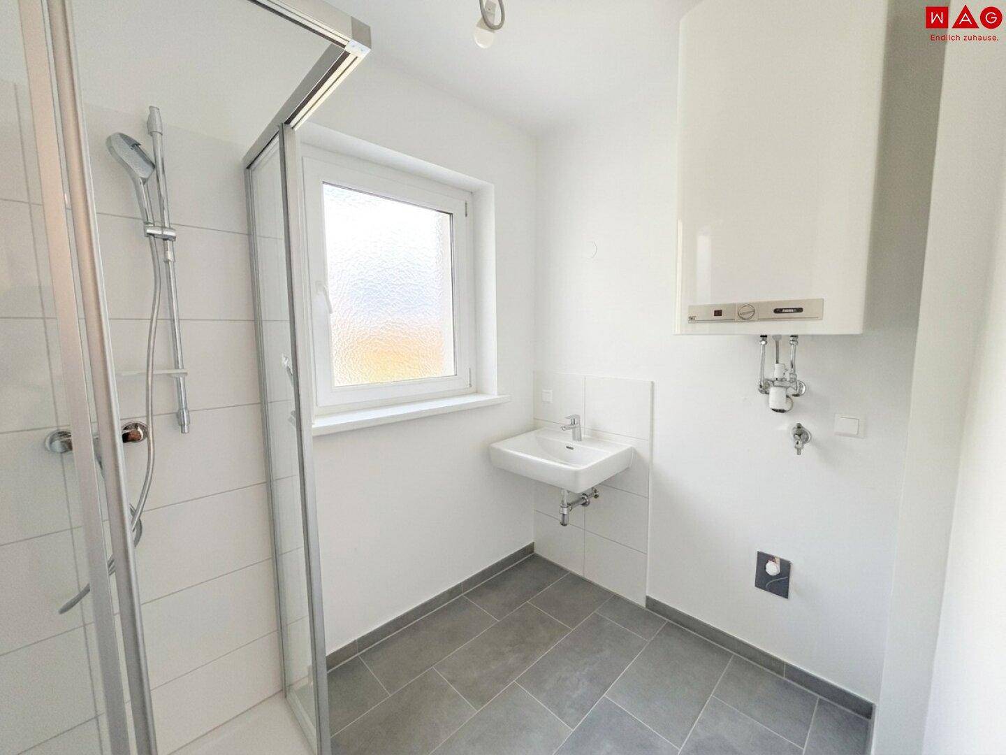 Modernes Badezimmer mit Dusche, kleinem Waschbecken, Fenster und Wandheizkessel.
