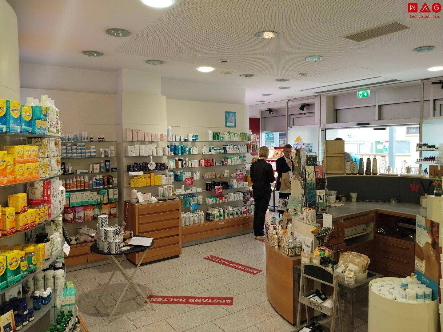 Innenansicht einer Apotheke mit gut gefüllten Regalen, Verkaufstheke und Kundenbereich.
