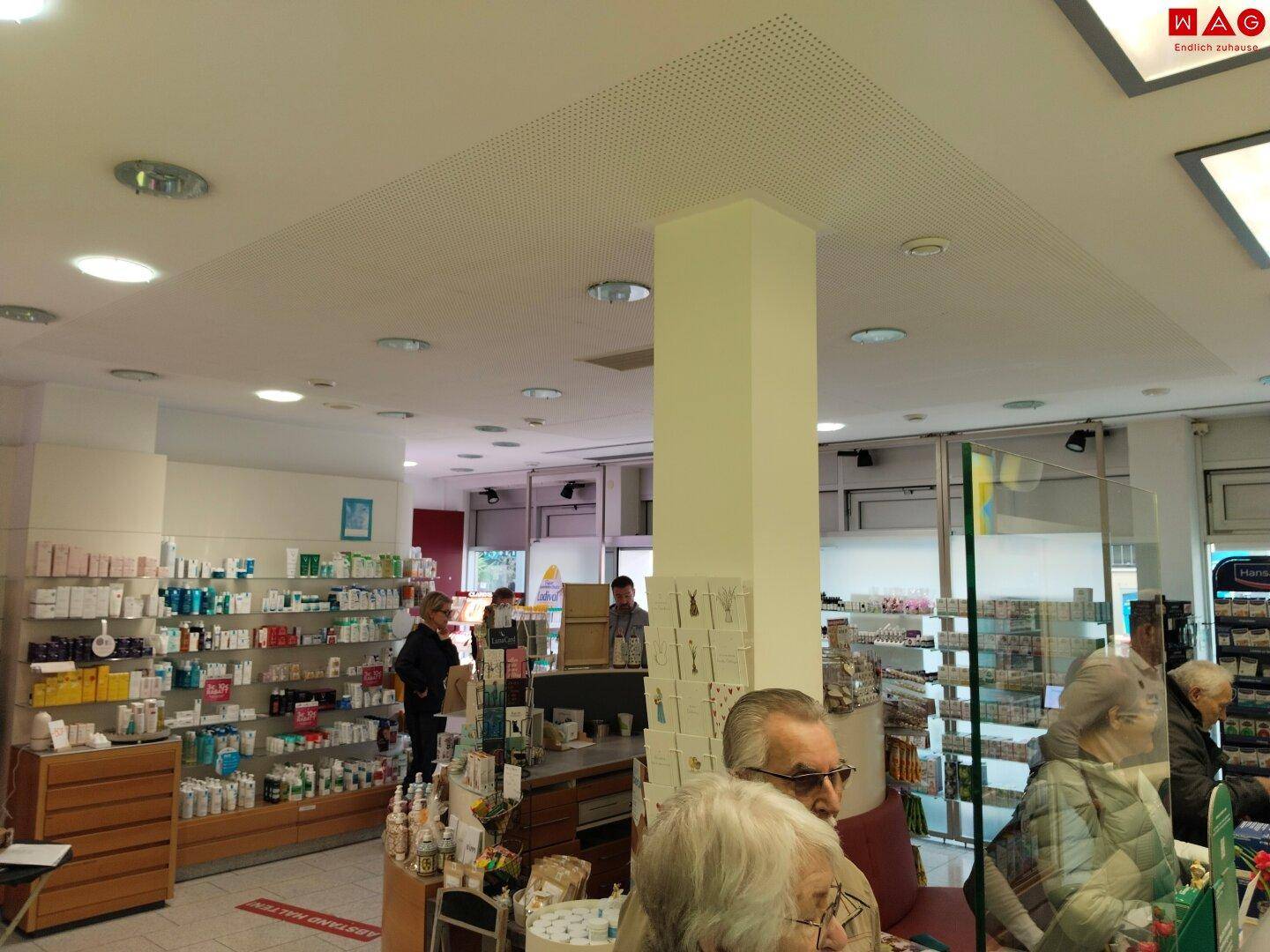 Innenansicht der Apotheke mit Deckenbeleuchtung, einem Pfeiler und weiteren Produktregalen.