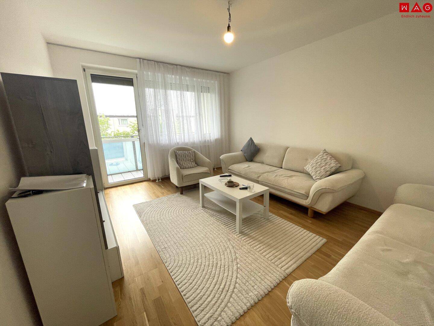 Gemütliches Wohnzimmer mit hellem Sofa, Holzboden und Zugang zu einem Balkon.