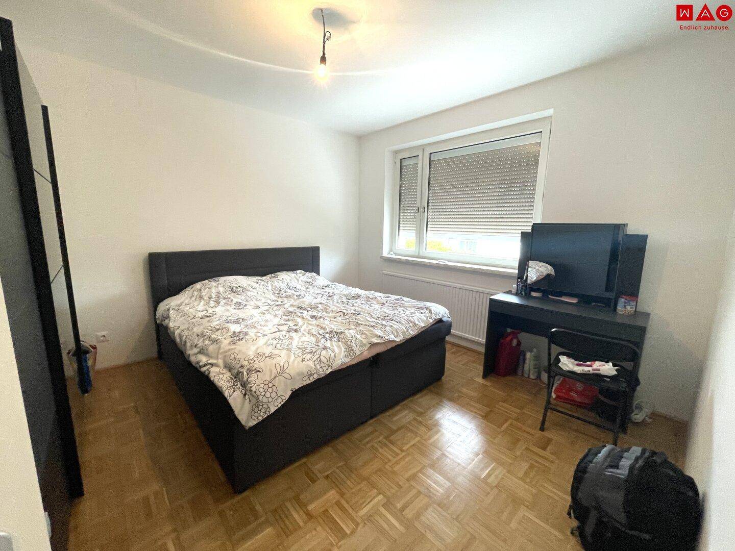 Schlafzimmer mit Doppelbett, Holzboden und einem Schreibtisch unter dem Fenster.