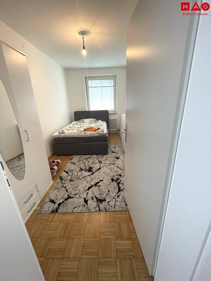 Kleines Schlafzimmer mit Einzelbett, Holzboden und einem Kleiderschrank mit Spiegel.