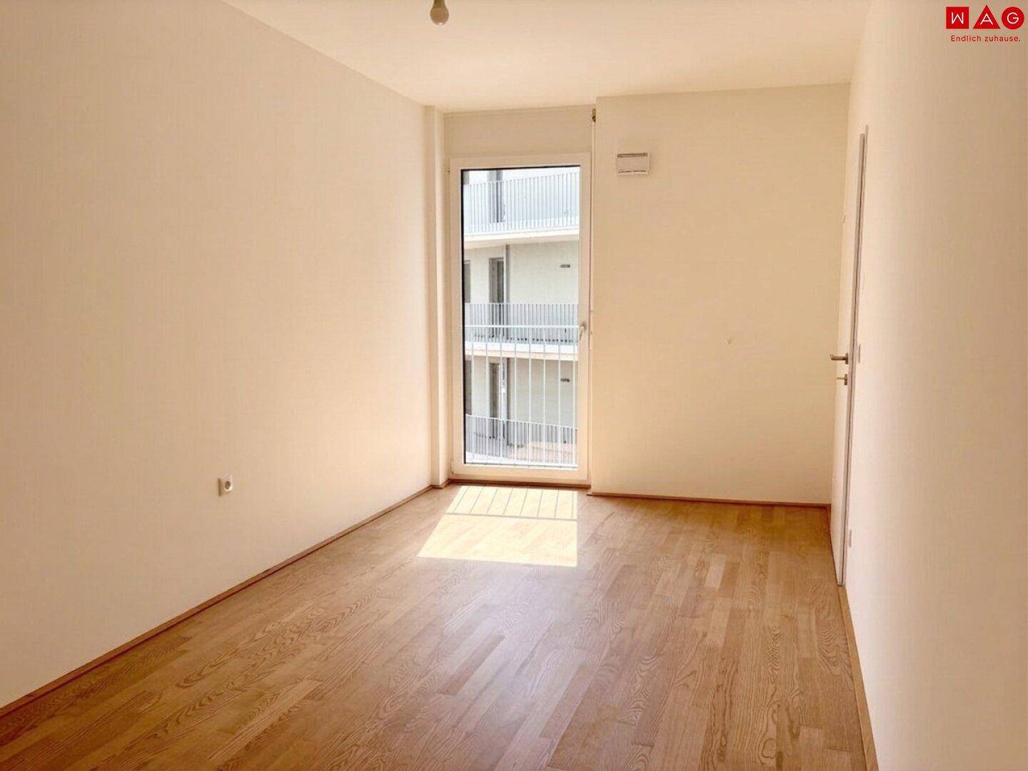 Unmöbliertes Schlafzimmer mit Holzboden und großem Fenster zum Balkon, lichtdurchflutet.