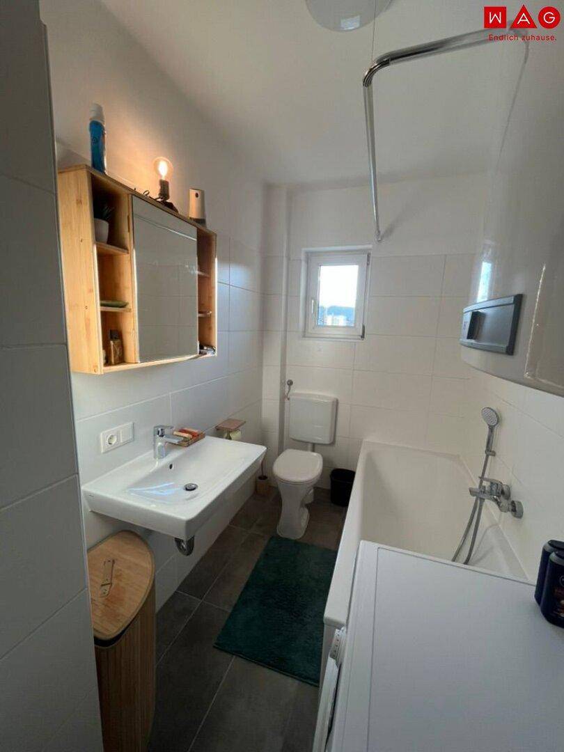 Helles Badezimmer mit Badewanne, WC, Waschbecken und einem Fenster für Tageslicht.