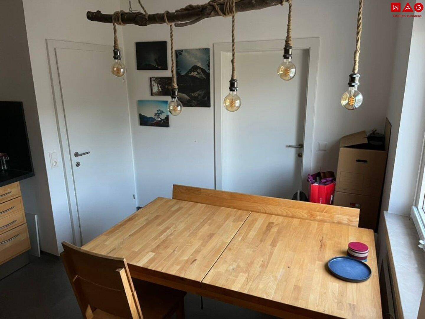 Essbereich in der Küche mit Holztisch und dekorativen Bildern an der Wand, neben zwei weißen Türen.
