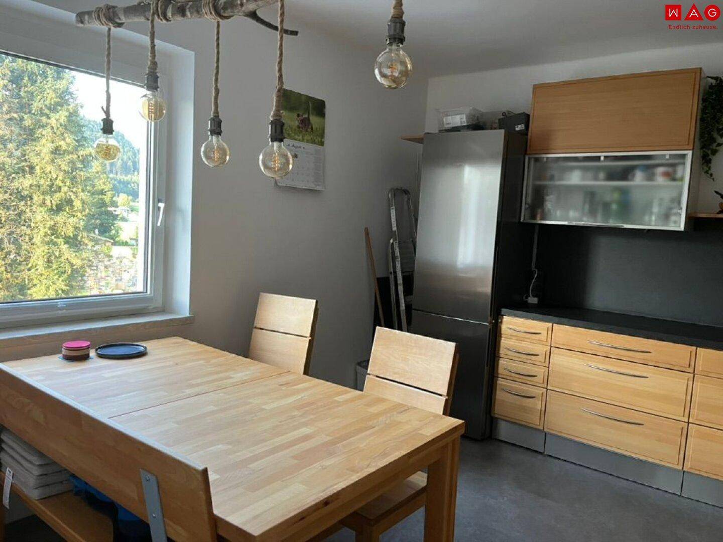 Heller Essbereich in der Küche mit Holztisch, Stühlen und Blick ins Grüne durch das Fenster.