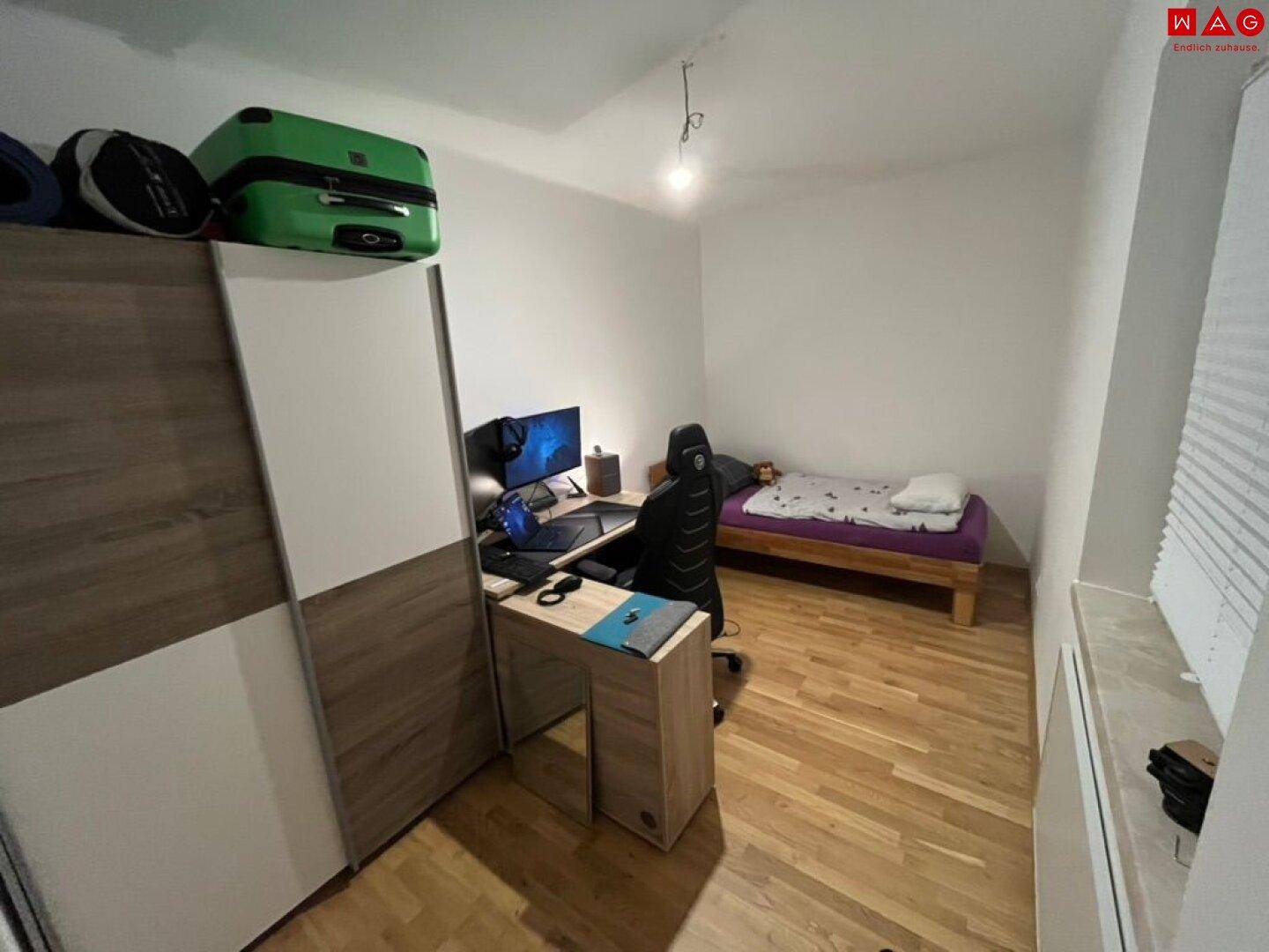 Schlafzimmer mit Holzboden, Schiebetürenschrank, Schreibtisch und einem Einzelbett.