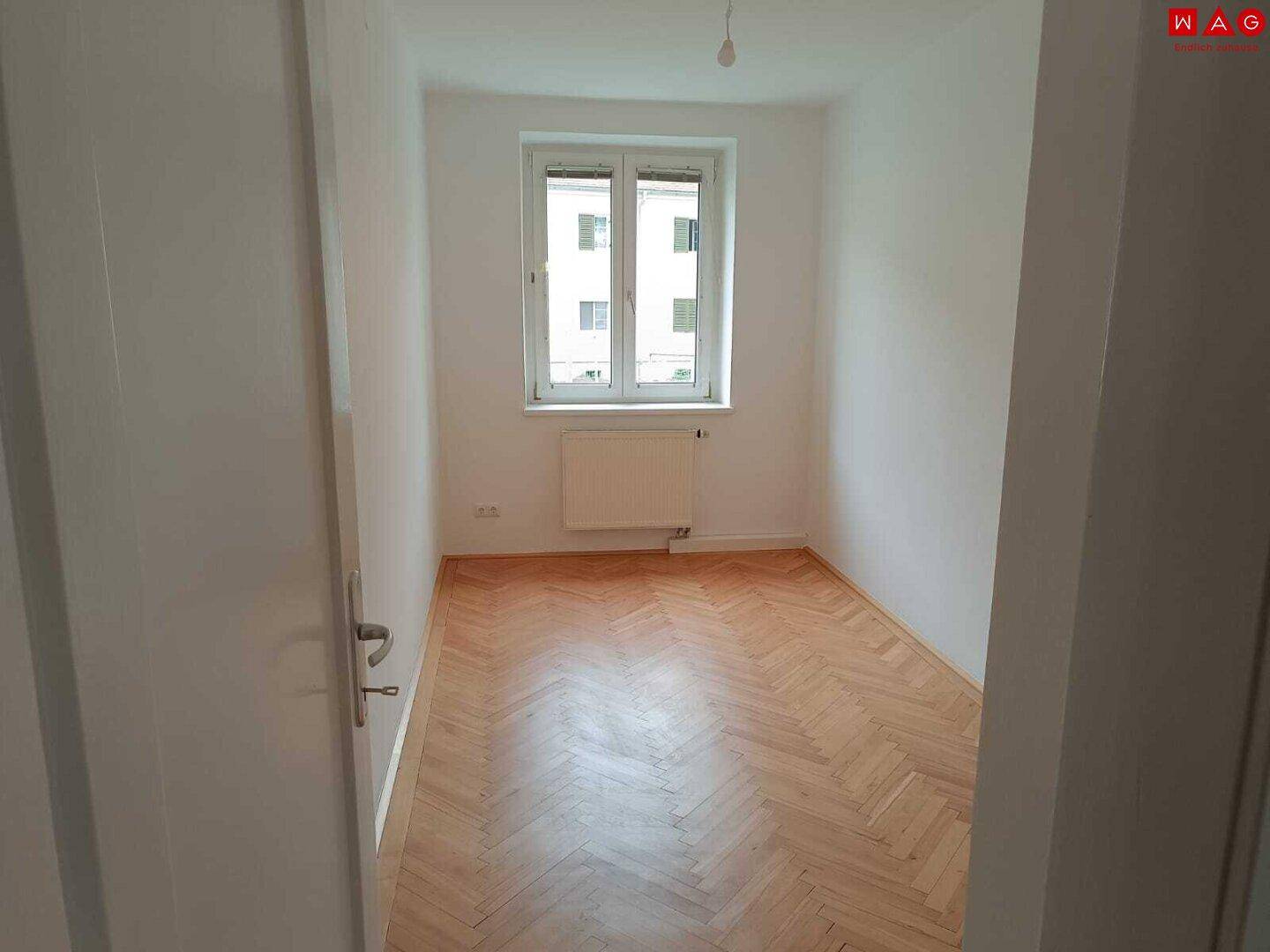 Kleineres, helles Zimmer mit Fischgrätparkett, einem Fenster und Heizkörper, geeignet als Kinder- oder Arbeitszimmer.