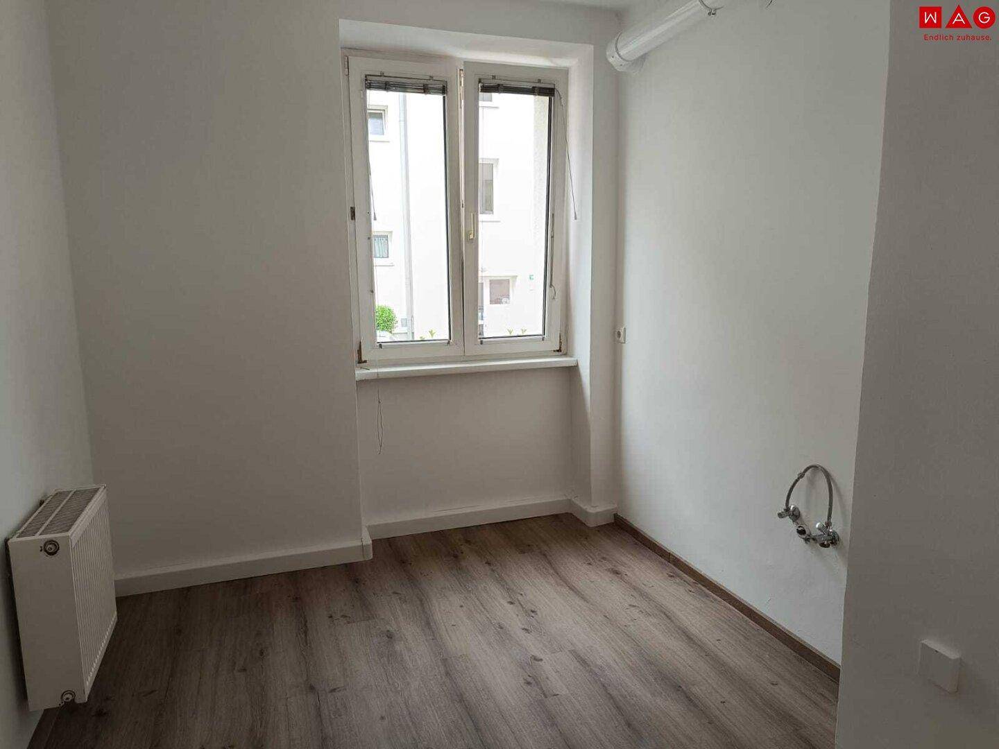 Funktionaler Raum mit Laminatboden, Fenster, Heizkörper und Wasseranschlüssen, ideal als Hauswirtschaftsraum.