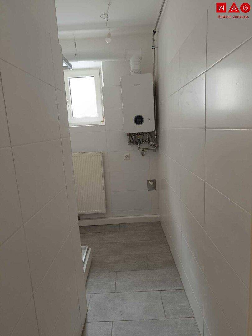 Gefliestes Badezimmer mit Fenster, Heizkörper und wandmontiertem Warmwasserbereiter, bietet gute Belüftung.