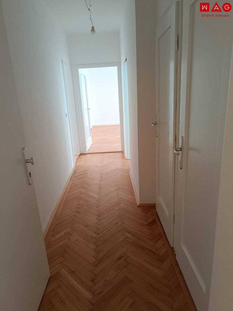 Heller Flur mit klassischem Fischgrätparkettboden und weißen Wänden, verbindet die verschiedenen Wohnbereiche.