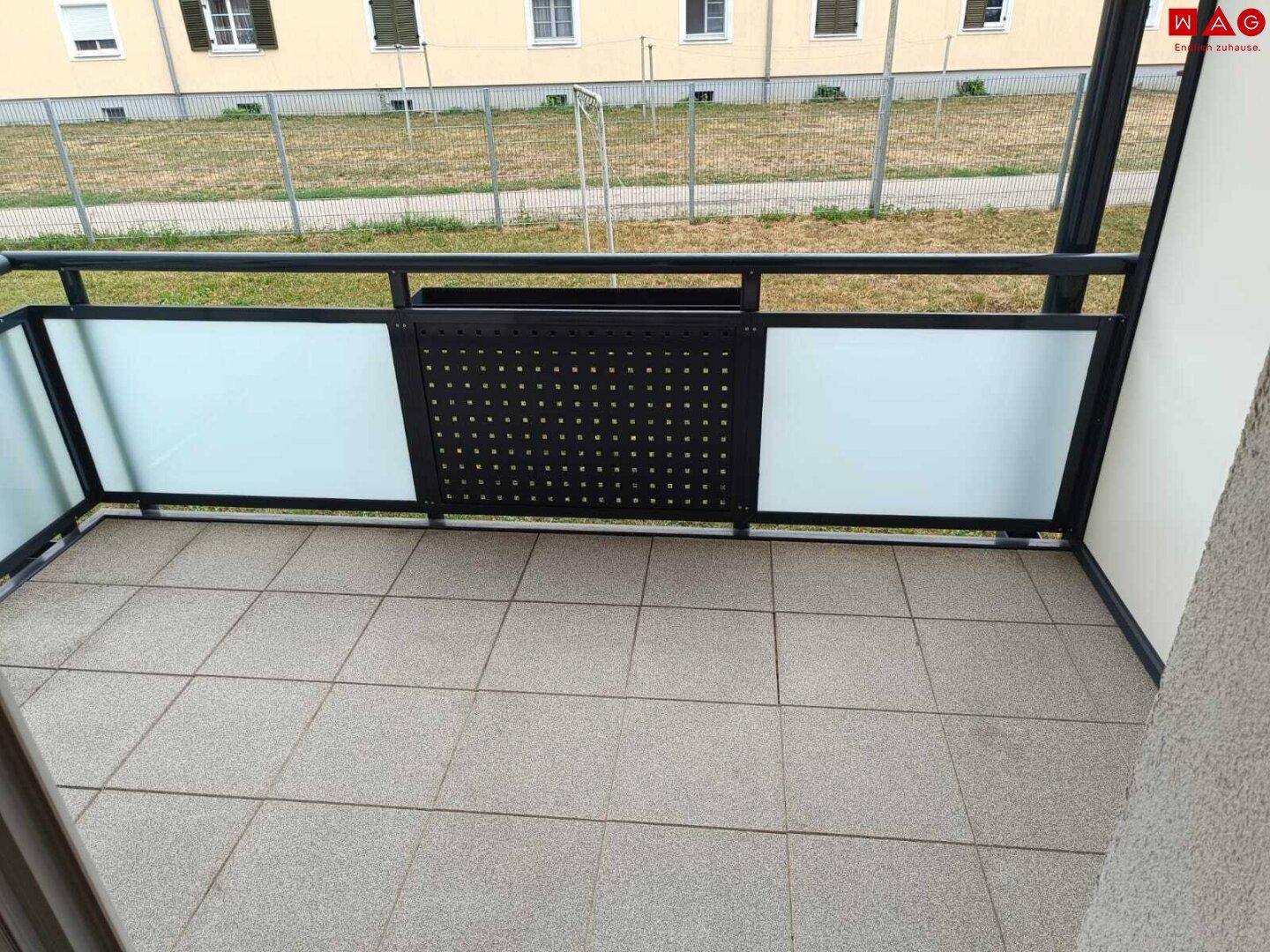 Geräumiger Balkon mit Fliesenboden und moderner Brüstung, bietet einen Blick ins Grüne.