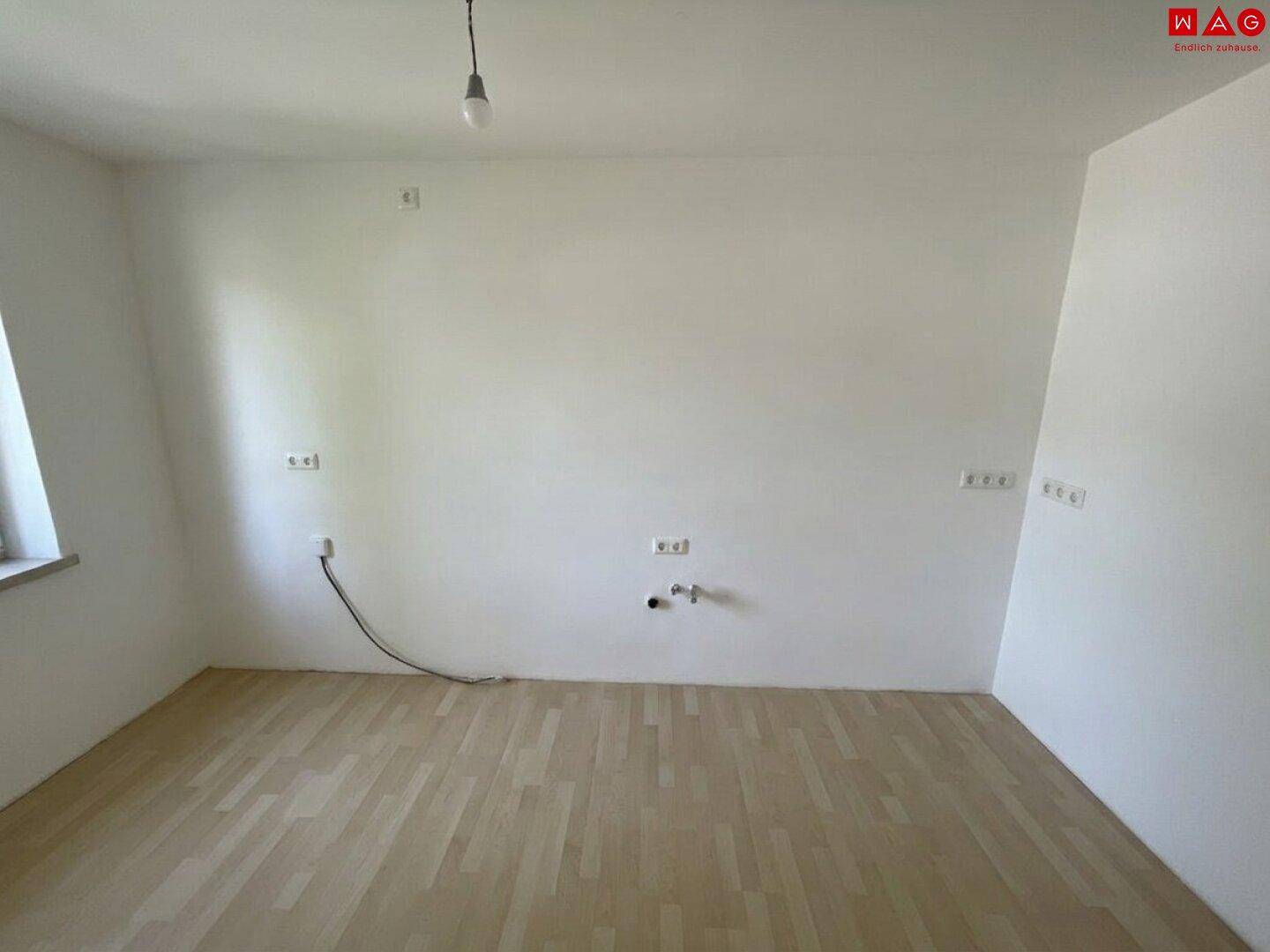 Leerer Raum, vorbereitet für eine Küche, mit hellem Laminatboden und Anschlüssen.