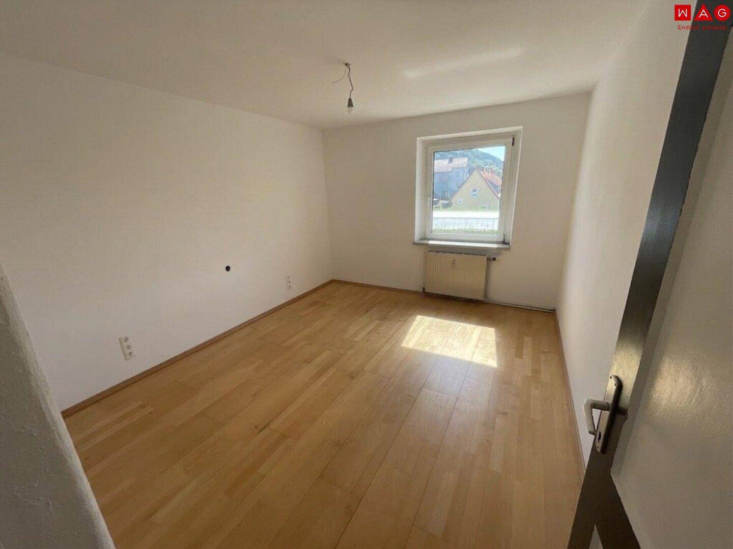 Helles Schlafzimmer mit Laminatboden, einem Fenster und viel Tageslicht.