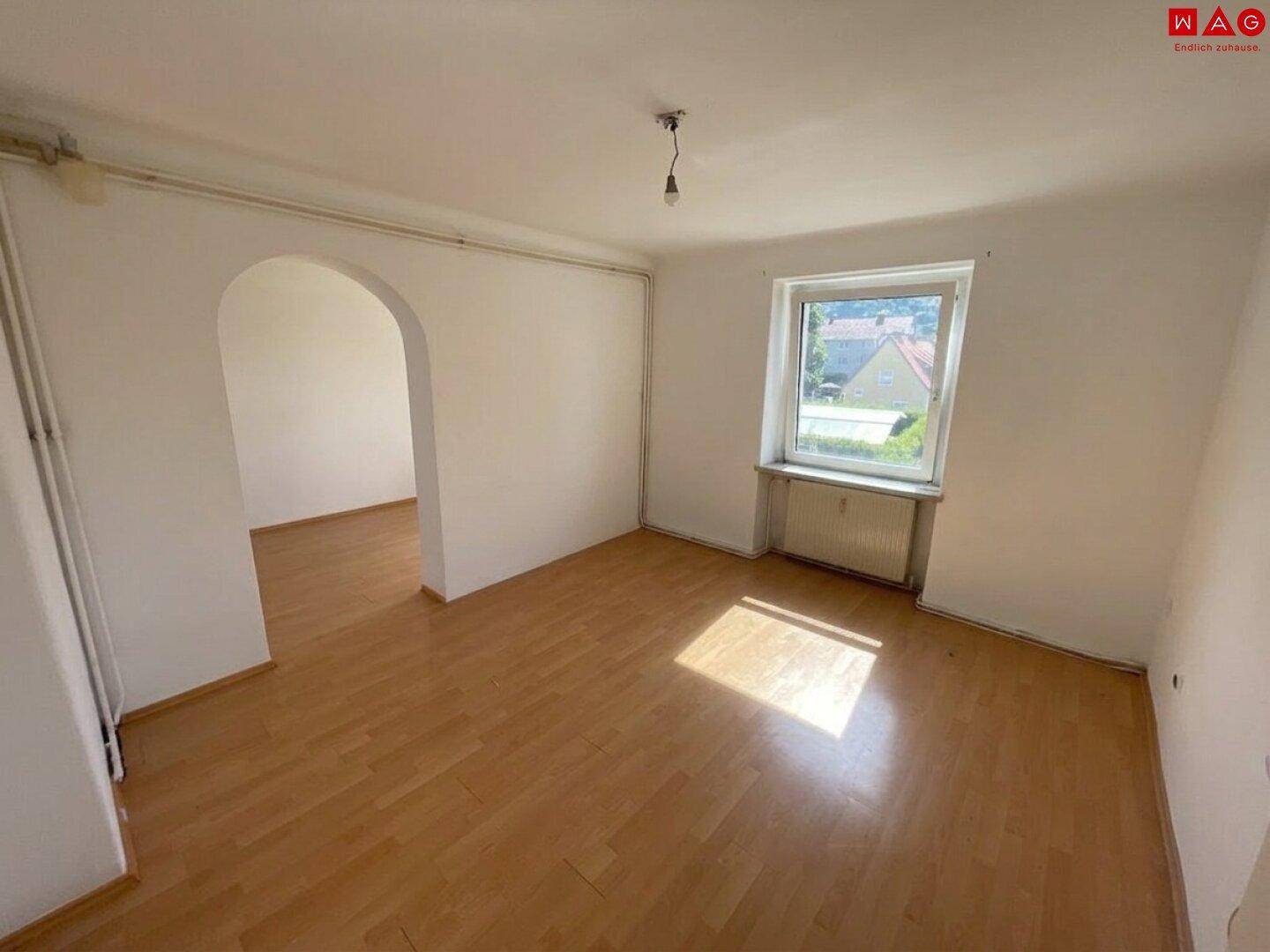 Heller Wohnraum mit Laminatboden, einem Rundbogen und Fenster mit Ausblick.