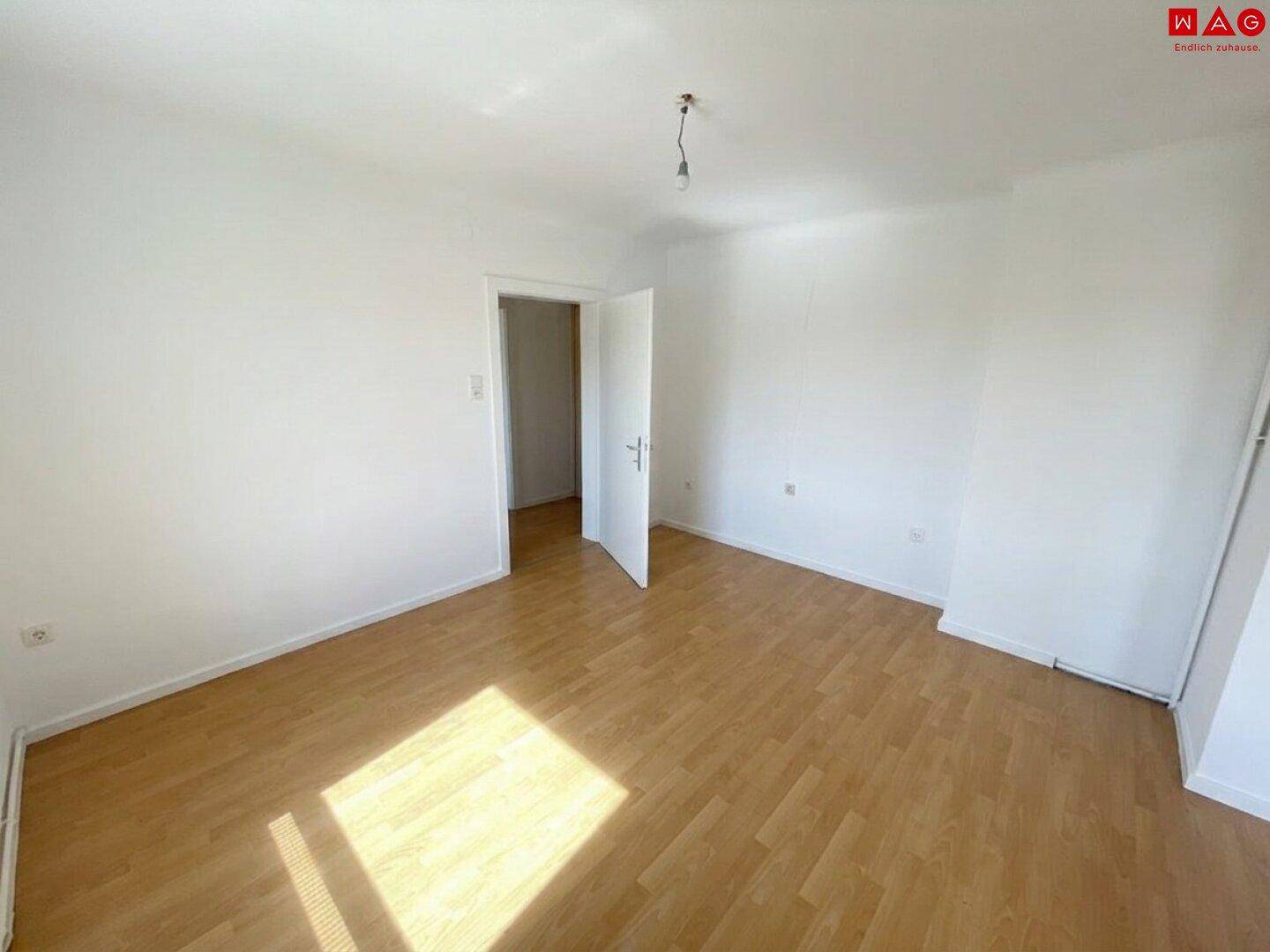 Geräumiges Schlafzimmer mit hellem Laminatboden und viel natürlichem Tageslicht.
