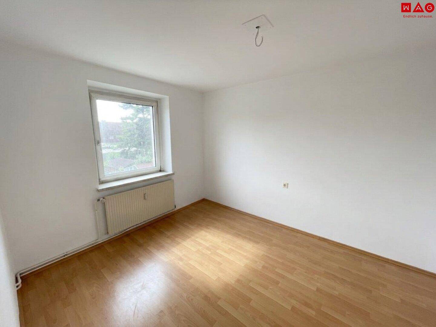 Helles Schlafzimmer mit Laminatboden, einem Fenster und einem Heizkörper.
