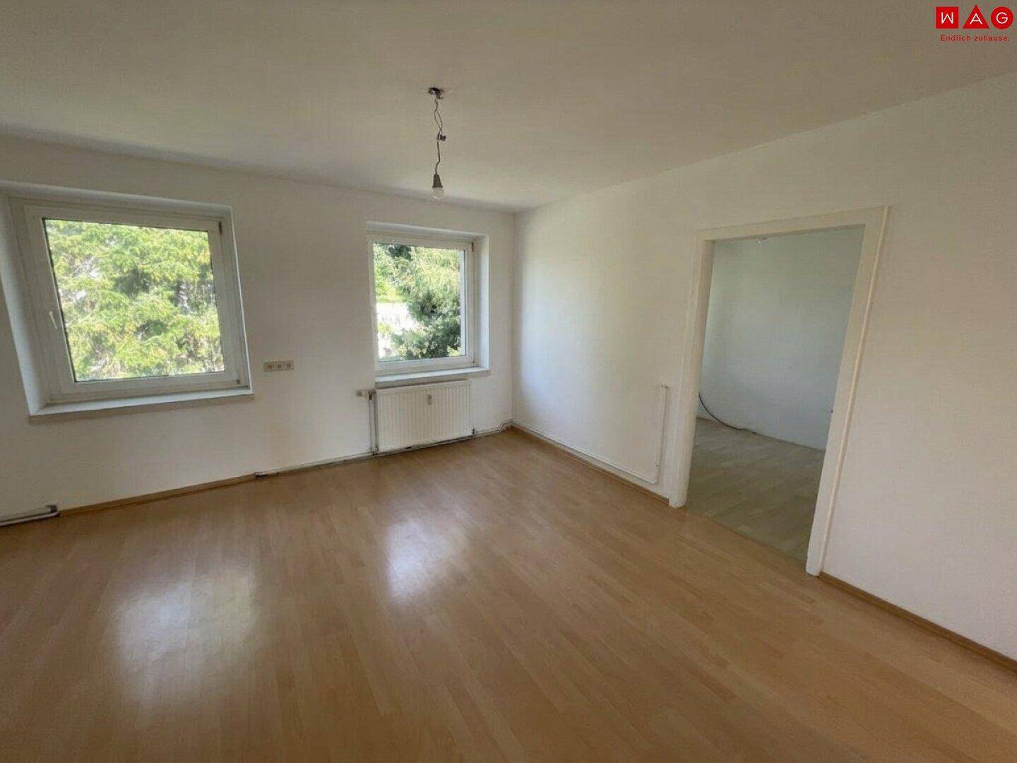 Heller Wohnraum mit zwei Fenstern, Heizkörper und hellem Laminatboden.