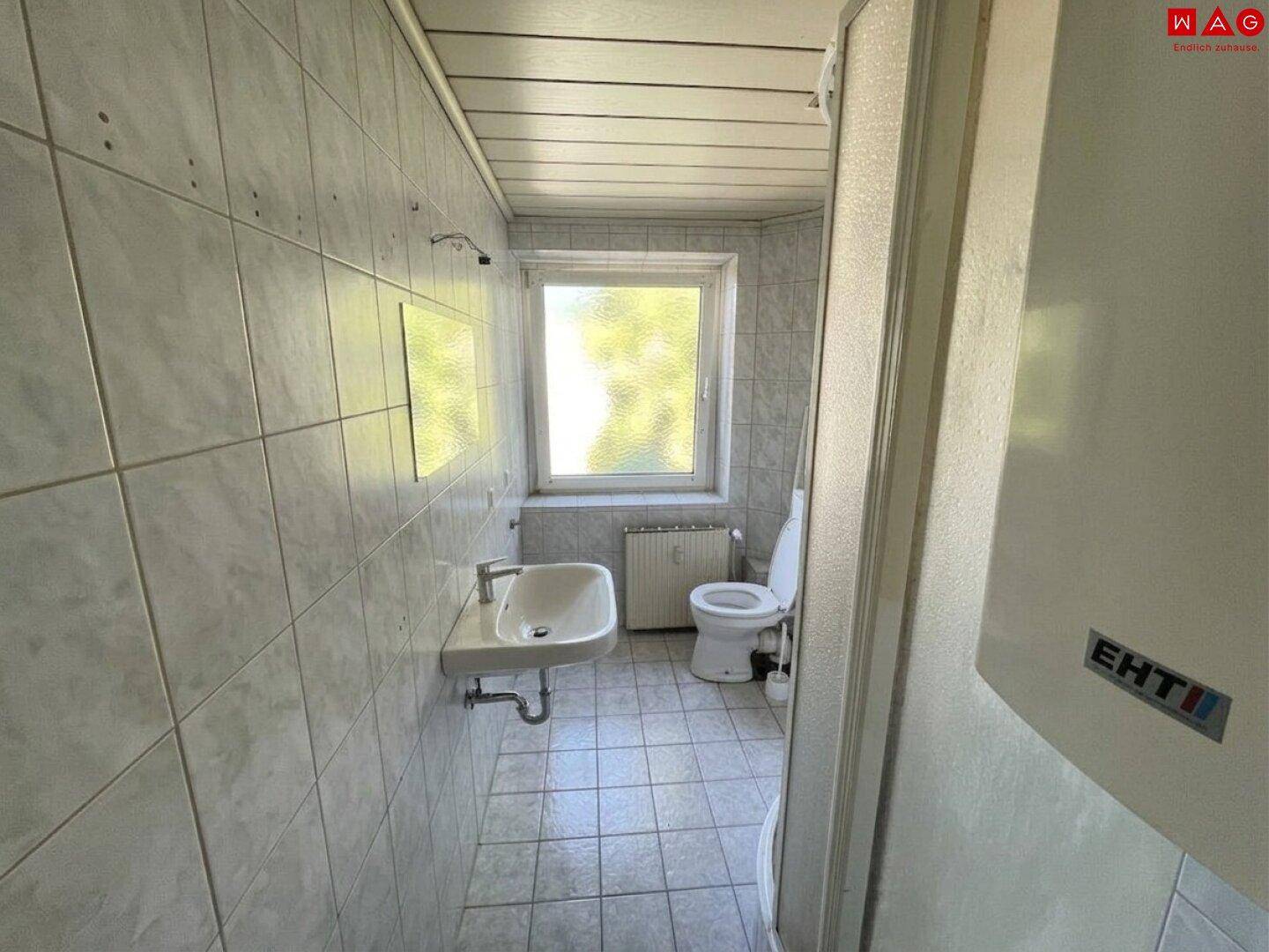 Funktionales Badezimmer mit hellgrauen Fliesen, Waschbecken, WC und Fenster.