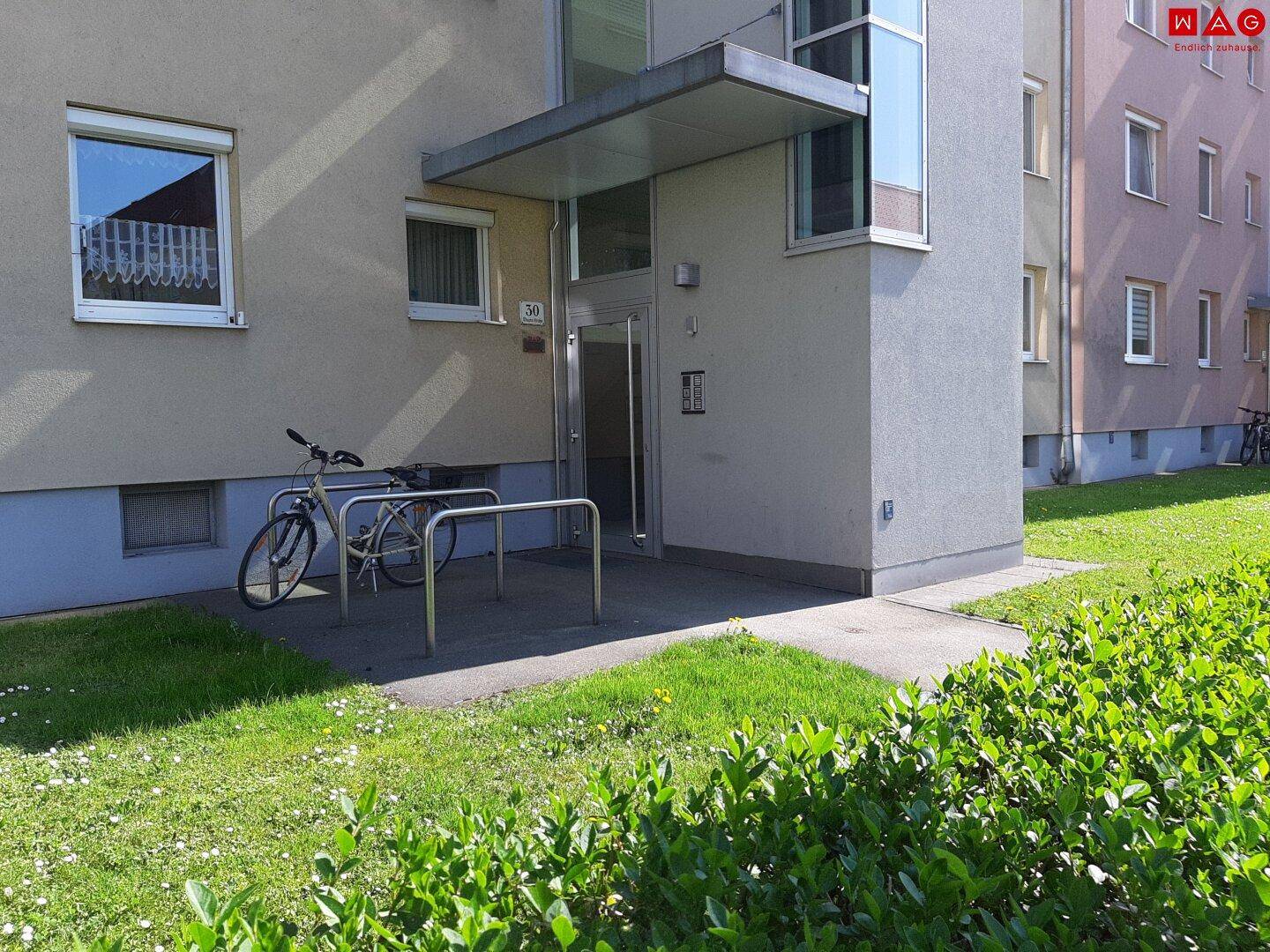 Eingangsbereich eines Mehrfamilienhauses mit Fahrradstellplätzen und gepflegtem Vorgarten.