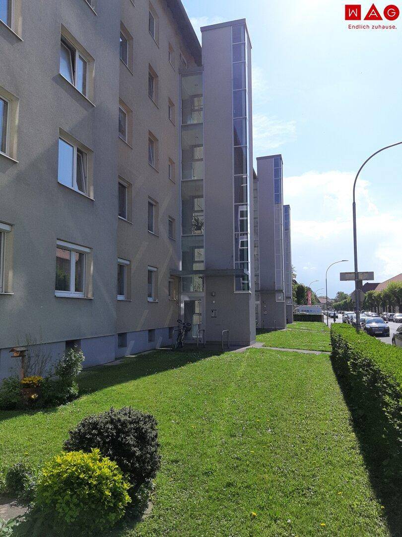 Modernisiertes Mehrfamilienhaus mit außenliegenden Glasaufzügen und gepflegter Grünfläche.