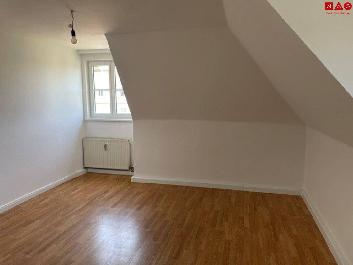 Lichtdurchflutetes Dachgeschosszimmer mit schrägen Wänden, Laminatboden und einem Fenster.