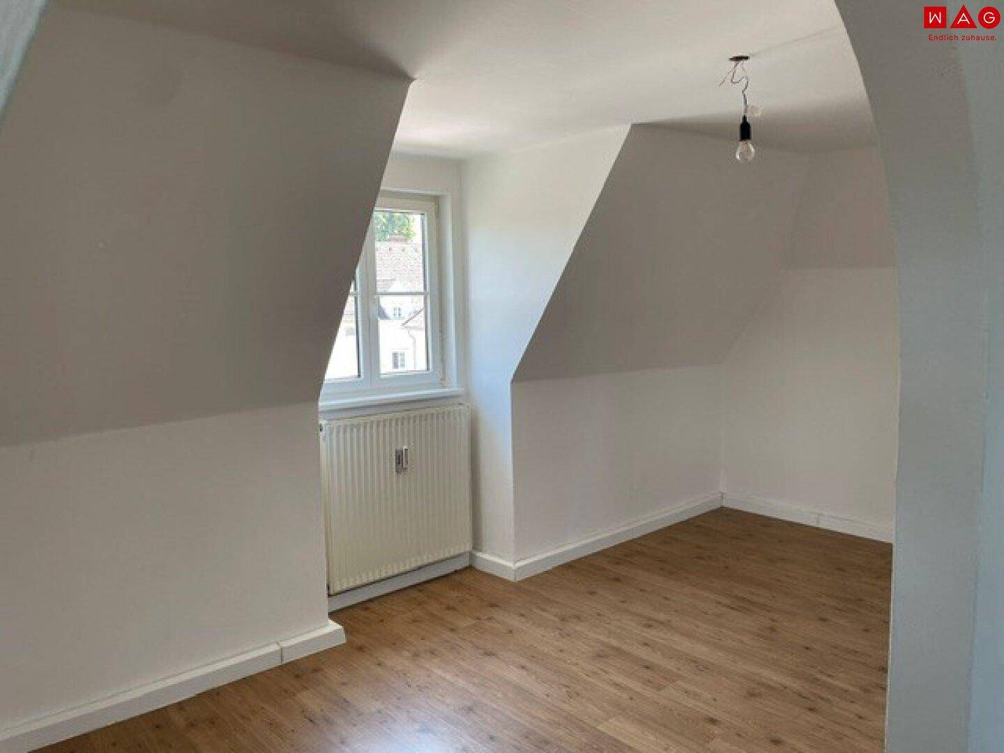 Helles Zimmer im Dachgeschoss mit Dachschrägen, Laminatboden und Fenster.