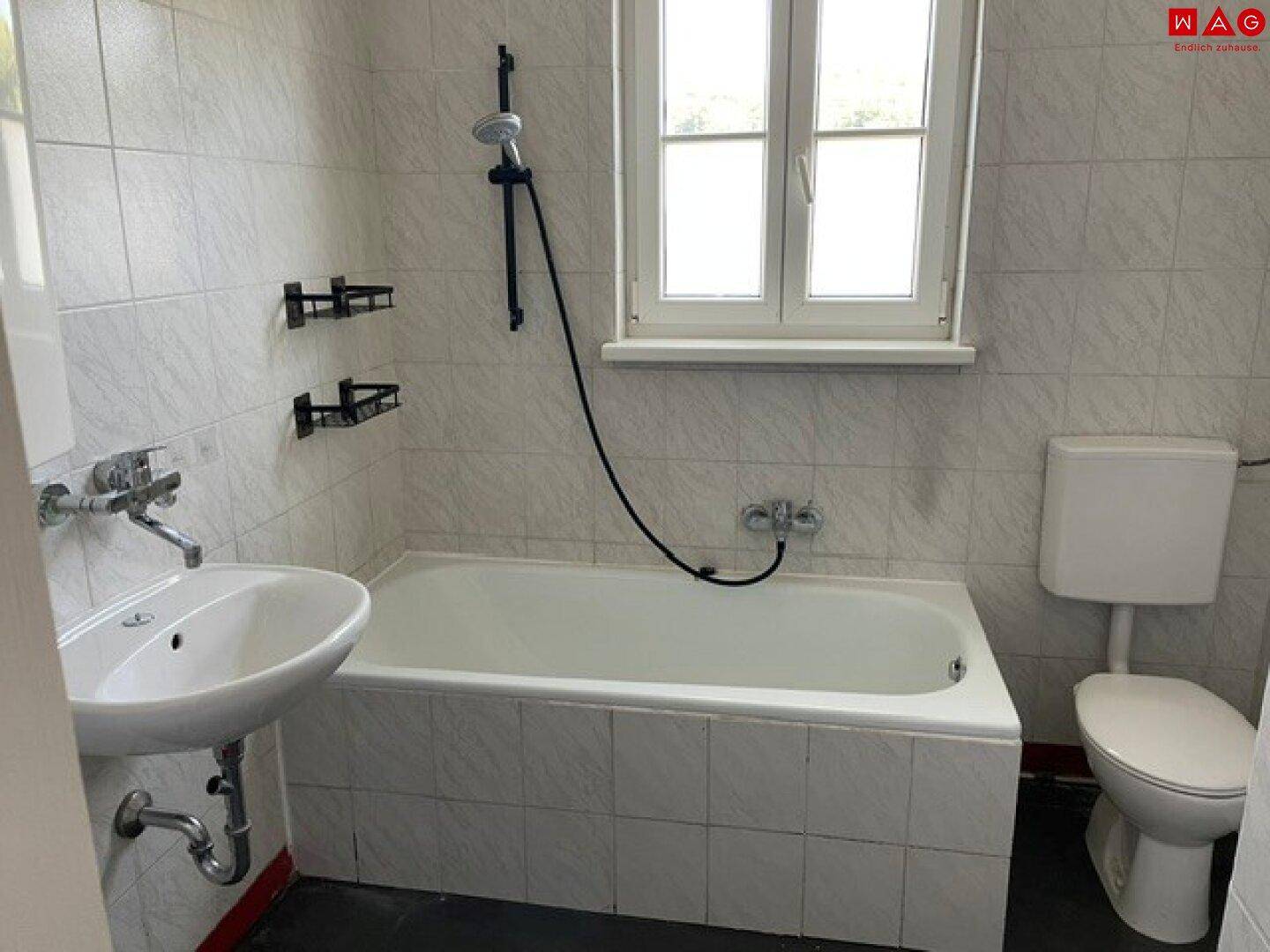 Gefliestes Badezimmer mit Badewanne, Waschbecken, Toilette und Fenster für Tageslicht.