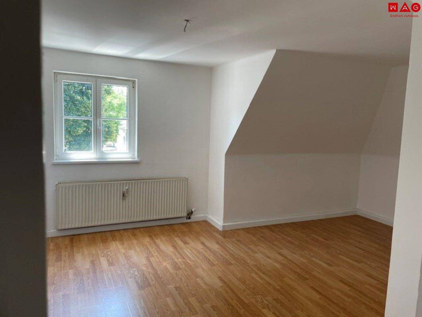 Geräumiges Zimmer im Dachgeschoss mit Laminatboden, weiß gestrichenen Wänden und Ausblick ins Grüne.