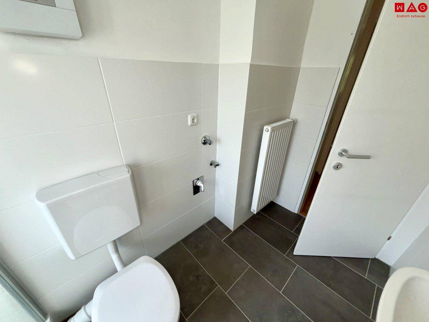 Detailansicht des Badezimmers mit WC, Heizkörper und weißen Wandfliesen.