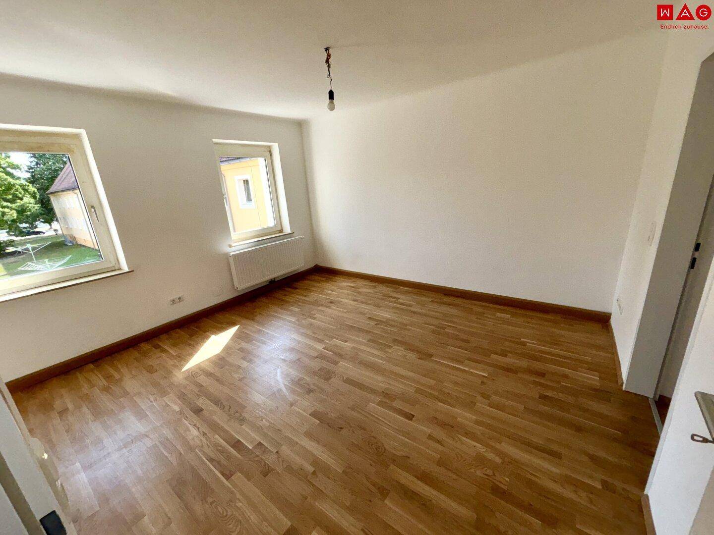 Leeres Zimmer mit Parkettboden und Blick ins Grüne durch das Fenster.