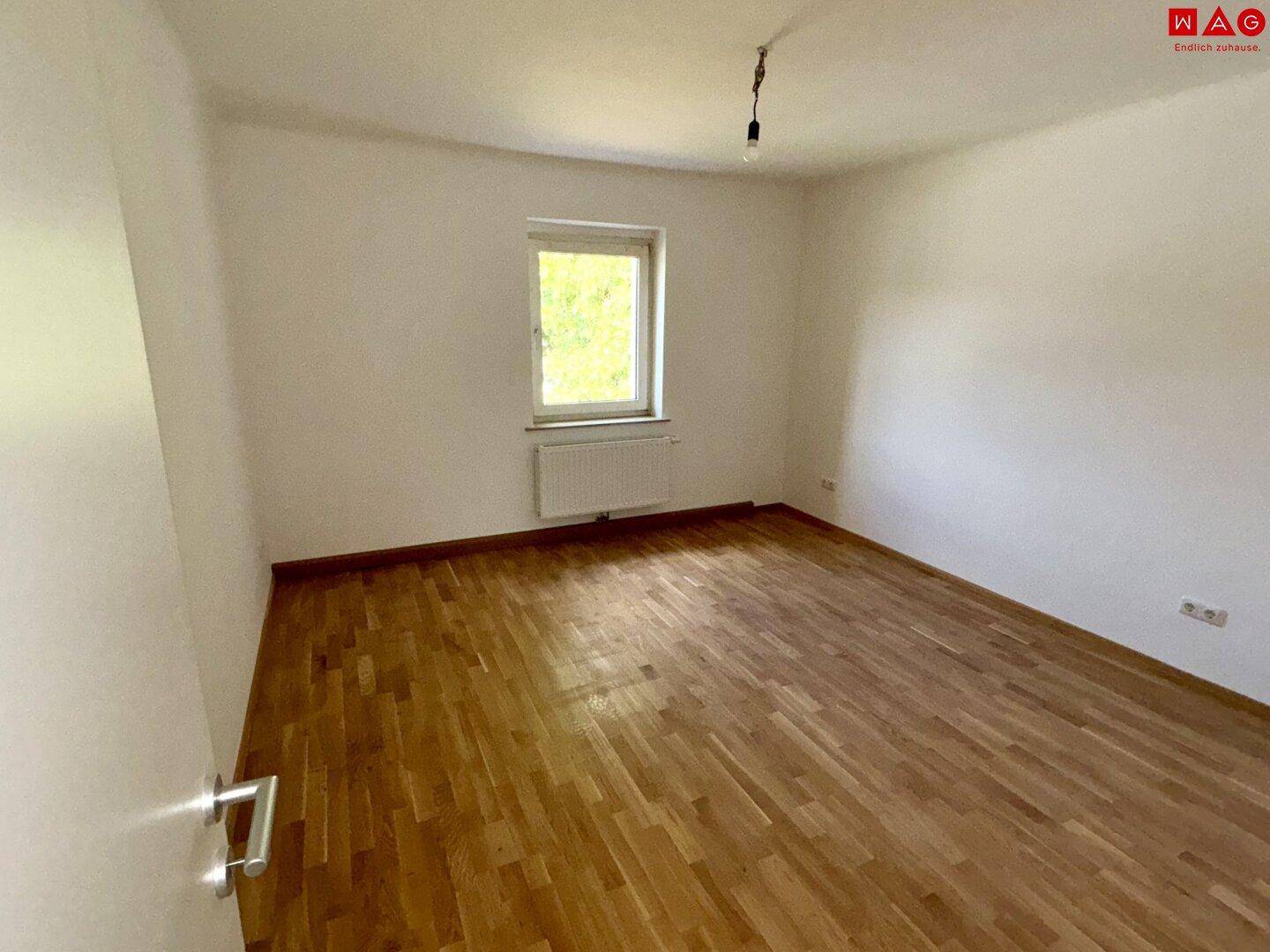 Helles Schlafzimmer mit Parkettboden und einem Fenster, das den Raum gut belichtet.