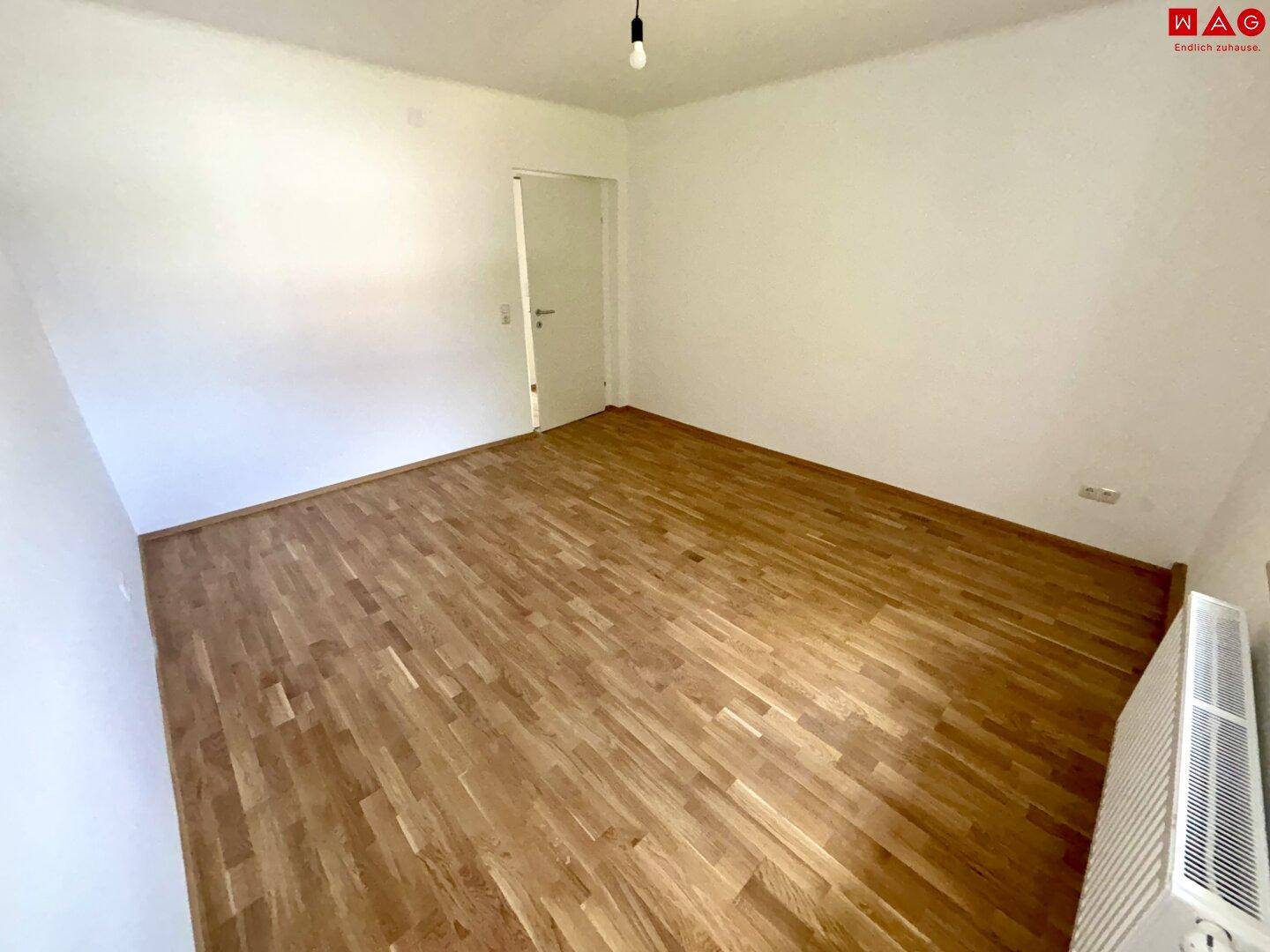 Leeres Schlafzimmer mit Parkettboden und Heizkörper, bereit für neue Bewohner.